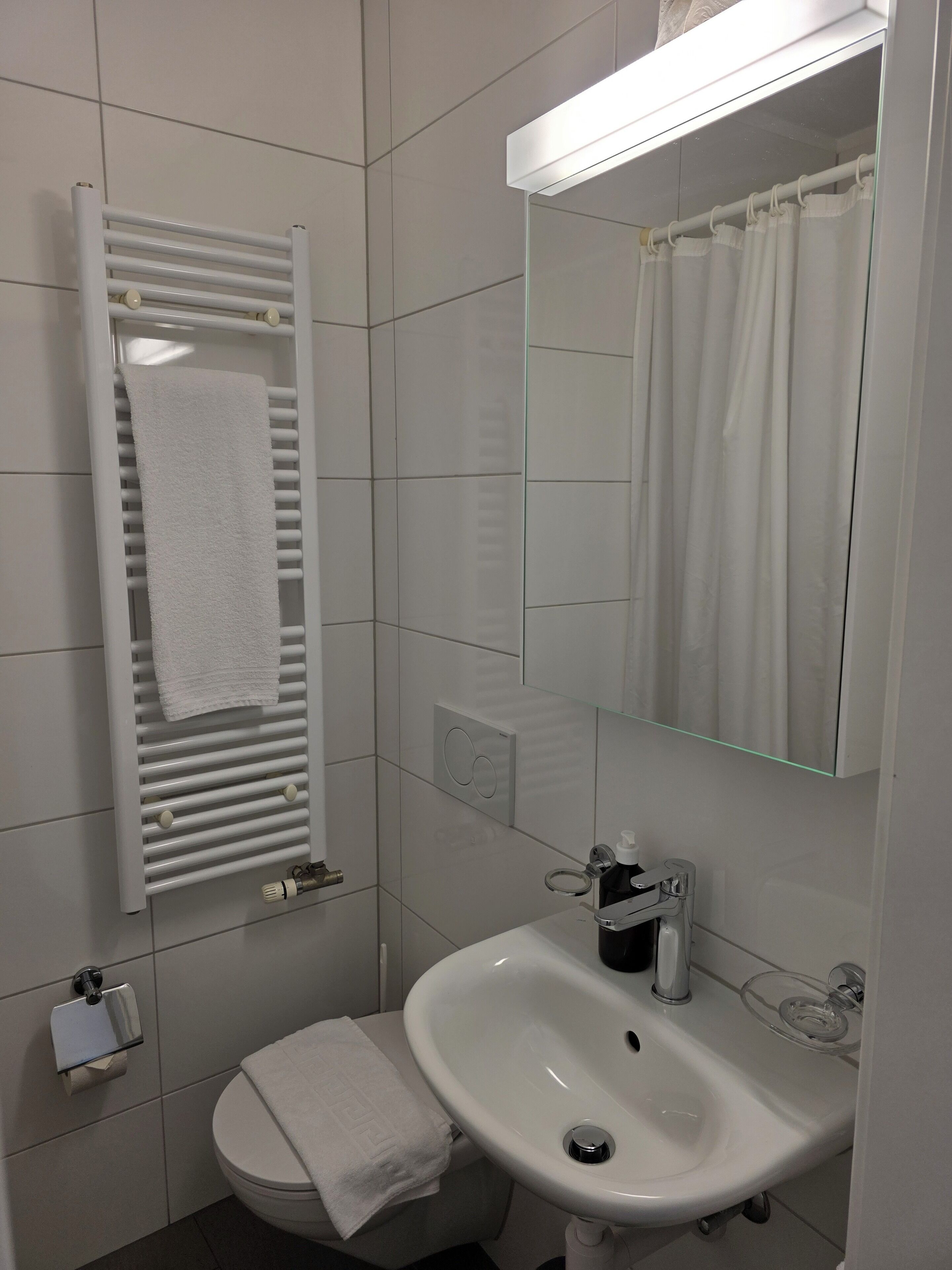 A modern bathroom with a white radiator, a sink, a toilet, and a mirror.