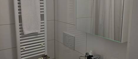 A modern bathroom with a white radiator, a sink, a toilet, and a mirror.