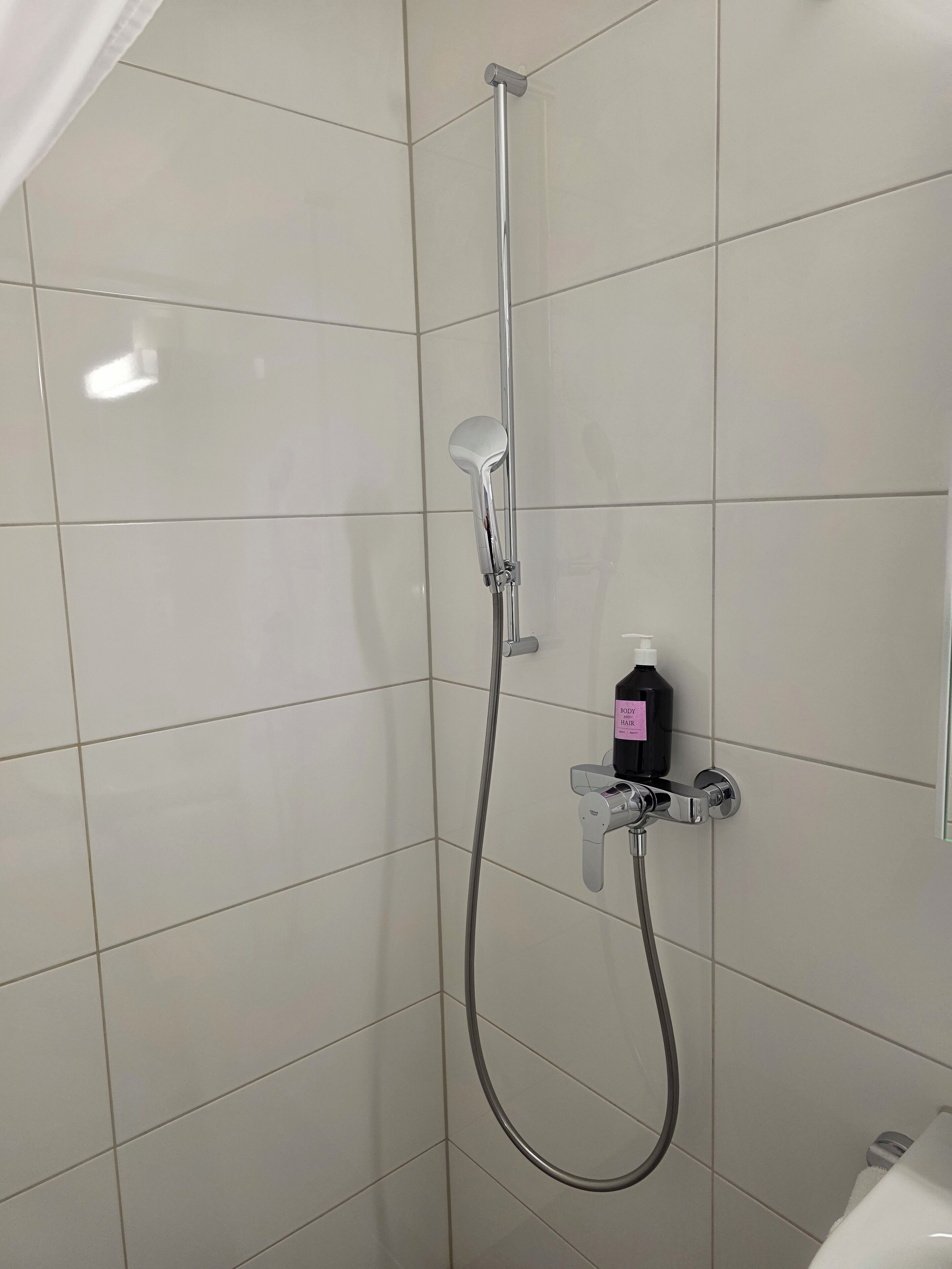 Ducha con cabezal de ducha de mano y grifo empotrado, una botella de champú y un perchero.