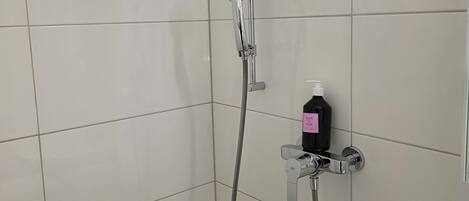Ducha con cabezal de ducha de mano y grifo empotrado, una botella de champú y un perchero.