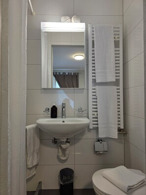 Une salle de bain avec un lavabo blanc, un miroir, un porte-serviettes et des toilettes.