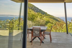 A dining area with a table and chairs, overlooking a scenic view of a coastline and hills. - Secluded villa, epic views, pool & sauna - 6 mins drive from town centre and pubic beach. (Brenzone sul Garda)