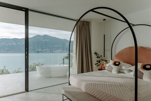 A bedroom with a large bed, a bathtub, and a view of a lake and mountains. - Secluded villa, epic views, pool & sauna - 6 mins drive from town centre and pubic beach. (Brenzone sul Garda)