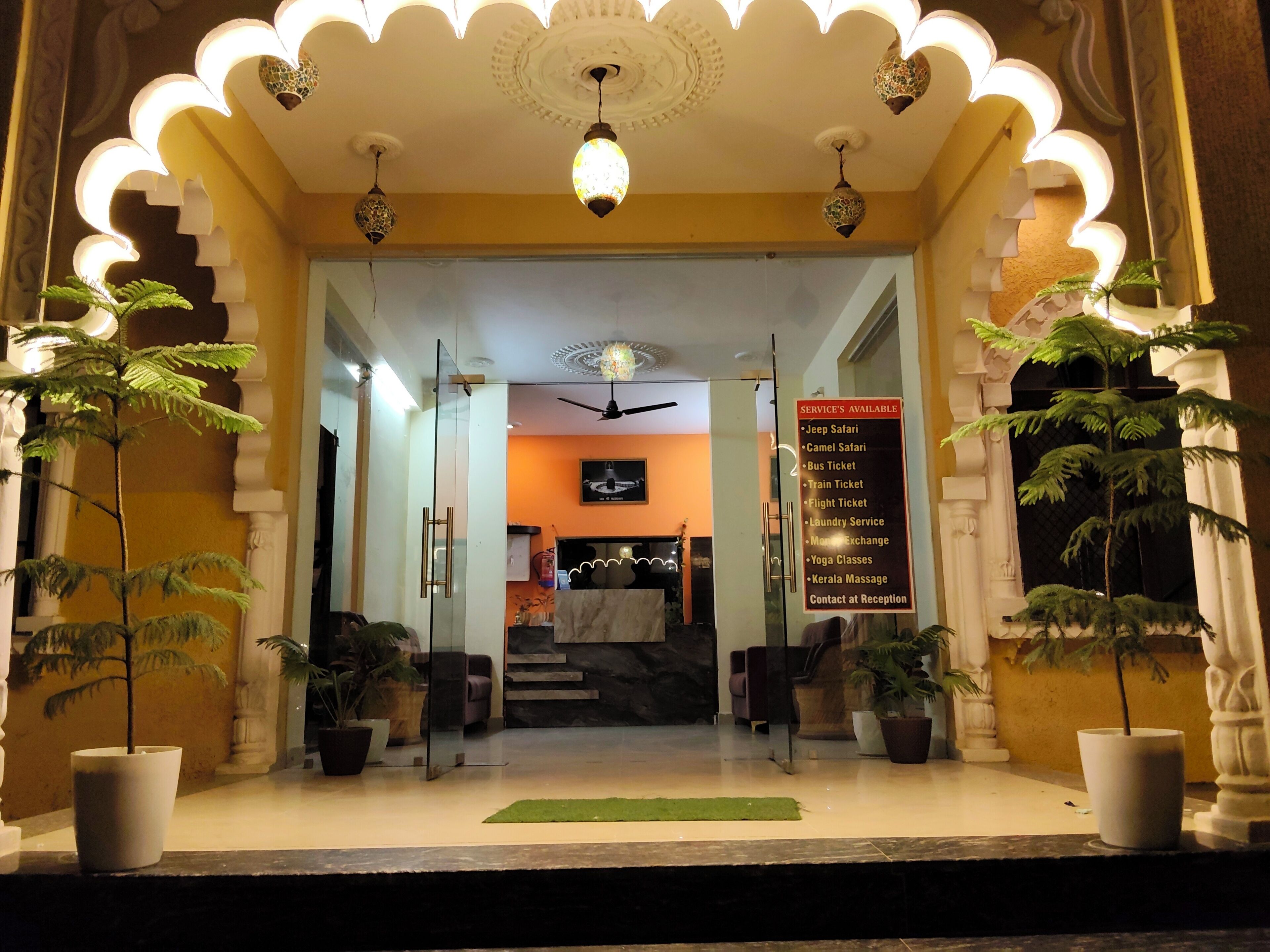 A hotel entrance with a reception desk, a list of services, and potted plants.
