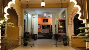 Ein Hotel Eingang mit einer Rezeption, einer Übersicht über die angebotenen Leistungen und einer Treppe zum Innenbereich.