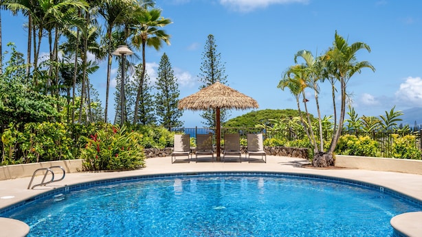 A swimming pool with lounge chairs and a thatched umbrella, surrounded by tropical plants and palm trees. - 🏝️ Maui is Calling - Beautiful Kapalua Ocean and Golf Course View (Lahaina)
