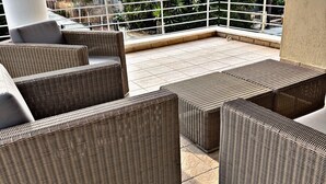 Ett takförsett utomhusområde med sittplatser, möbler av rotting och utsikt över de omgivande byggnaderna och träden.
