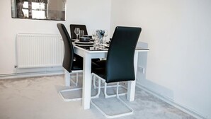 Un coin repas avec une table blanche, des chaises noires et un radiateur blanc.