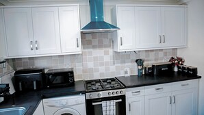 Une cuisine de taille réduite avec des meubles blancs, un micro-ondes noir, une cuisinière à gaz et un lave-linge.