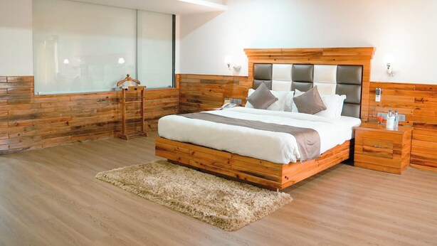 Un dormitorio con cabecera de madera, un ventanal grande, una mesita de noche y una alfombra mullida.