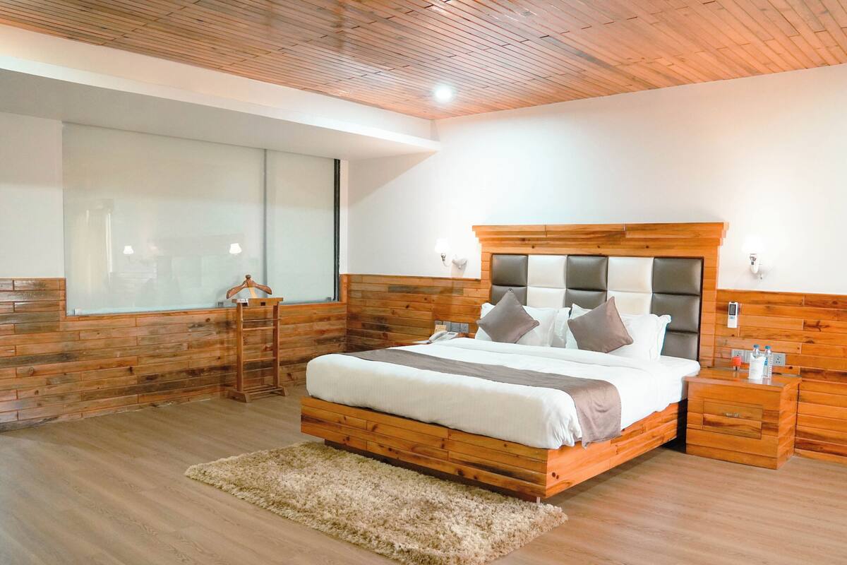 Une chambre à coucher avec une tête de lit en bois, une grande fenêtre, une table de chevet et un tapis moelleux.