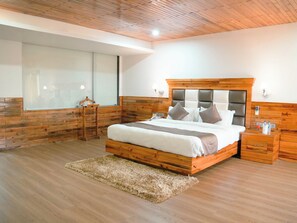 A bedroom with a wooden headboard, a large window, a bedside table, and a fluffy rug.