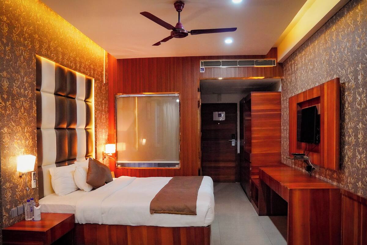 Une chambre d’hôtel avec un lit, des tables de chevet, un ventilateur de plafond, une télévision et une fenêtre.