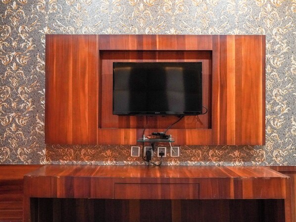 A wall-mounted TV in a wooden cabinet with a patterned wallpaper background.