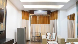 Una sala moderna con una televisión de pantalla plana, un refrigerador, un comedor con mesa y sillas, y un sofá con un cojín floral.