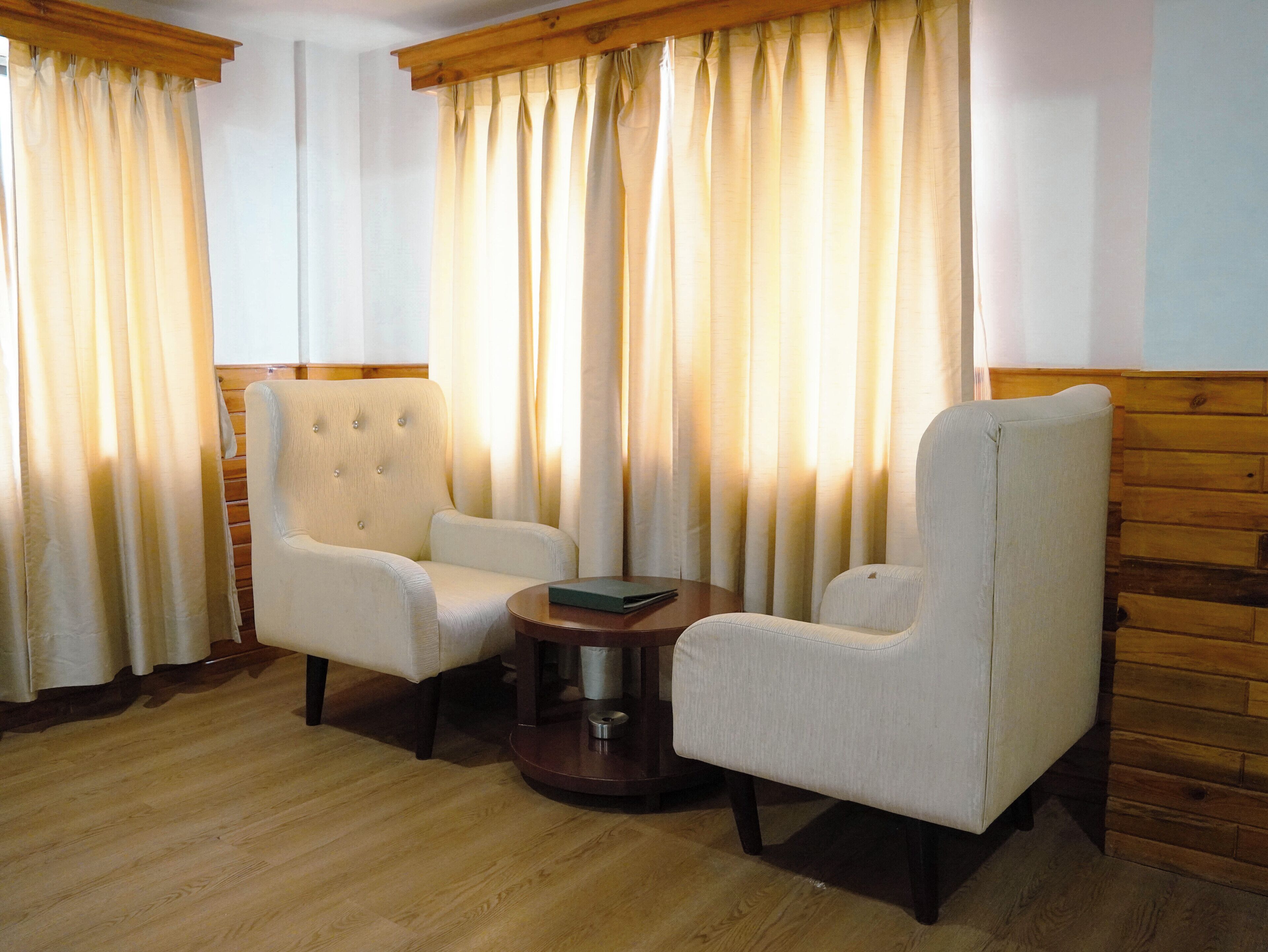 Una habitación con dos sillones tapizados, una mesa de madera y un ventanal con cortinas.