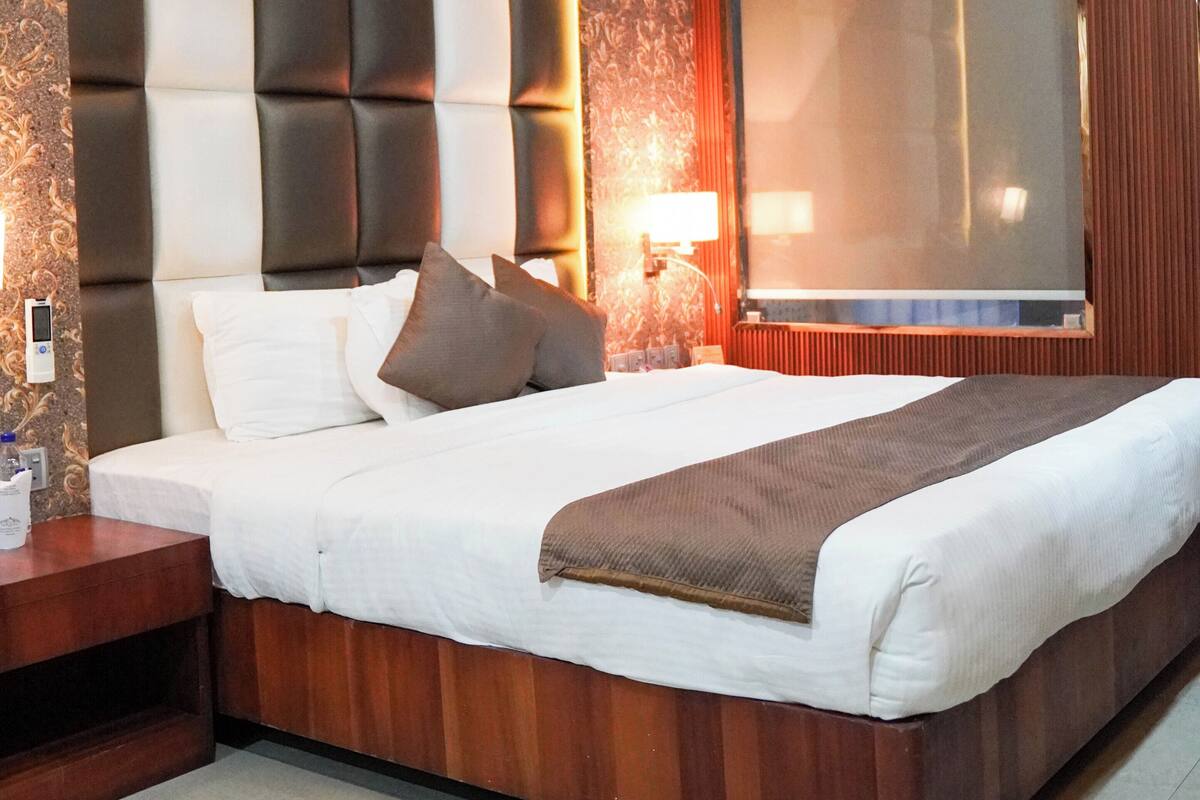 Une chambre d’hôtel avec un grand lit, une table de chevet, une commode, un téléviseur fixé au mur et un papier peint à motifs.
