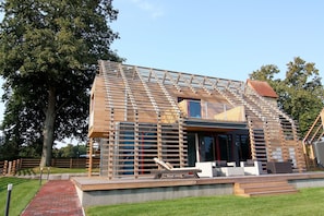 Una casa moderna con rivestimento in legno, un grande albero sullo sfondo e un patio con mobili da esterno.