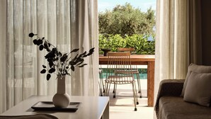 Une pièce comprenant une table à manger, un canapé, un vase avec des feuilles foncées, et donnant sur une piscine et un espace verdoyant à l’extérieur.