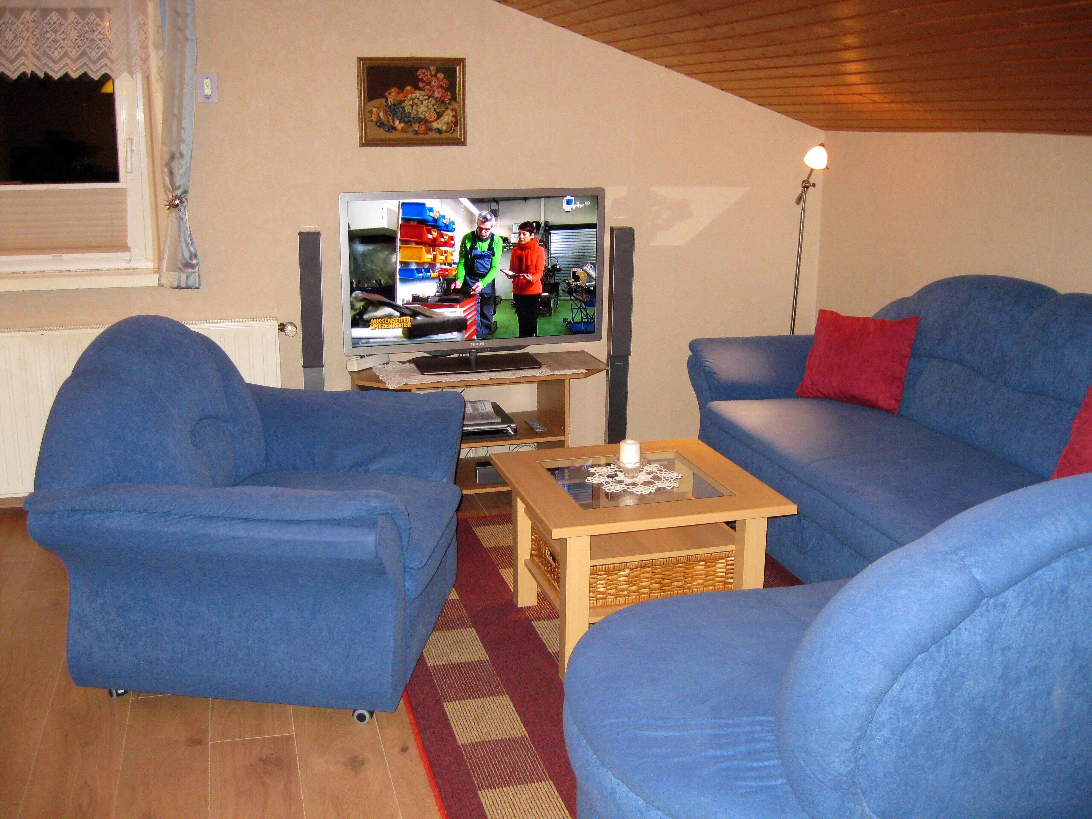 Una sala de estar con televisión, sofás azules y una pequeña mesa.