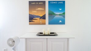 Un meuble blanc orné de deux affiches encadrées, un ventilateur blanc et trois bougies disposées sur un plateau.