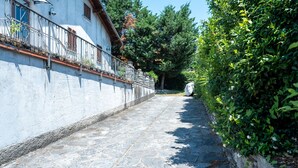 Un chemin pavé de pierres, bordé d’un bâtiment blanc doté d’une rambarde en métal et d’un mur de pierre d’un côté.