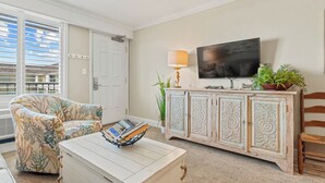 A living room with a sofa, a coffee table with a magazine, a TV, a cabinet, and a plant.