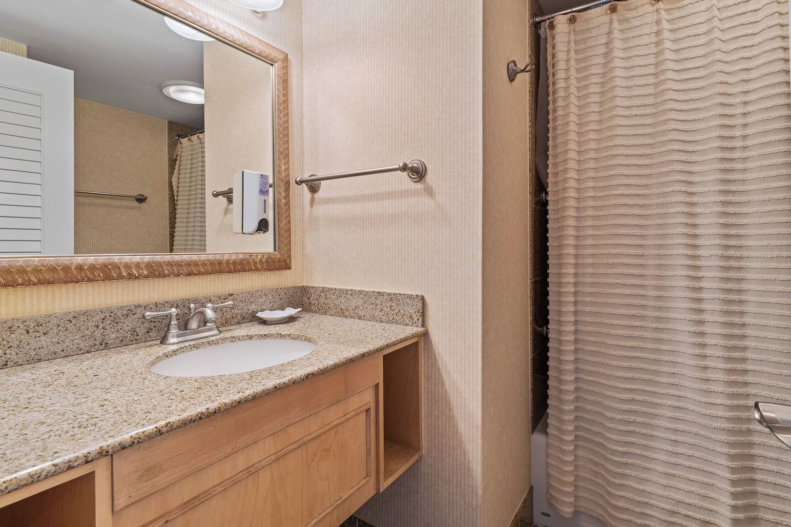 A bathroom with a granite countertop sink, a mirror with a decorative frame, a towel rack, and a shower curtain.