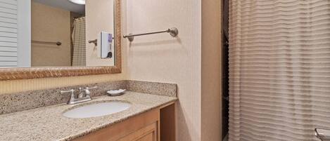 A bathroom with a granite countertop sink, a mirror with a decorative frame, a towel rack, and a shower curtain.