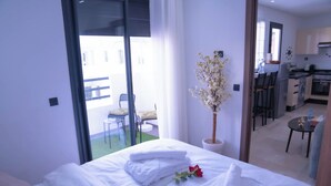 A hotel room with a bed, a potted plant, and a view of the balcony and kitchen.