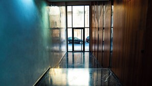 A hallway with a reflective marble floor, wooden walls, and a view of parked cars outside.