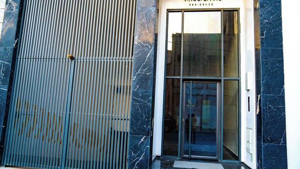 A modern building entrance with a metal gate, a glass door, and a sign reading "VINCOLI LIVING RESIDENCE".