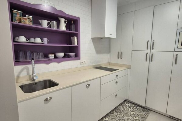 A kitchen with a sink, white cabinets, and a purple shelf with kitchenware.