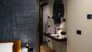 Ein modernes Hotelzimmer mit einem großen Bett, einem Nachttisch, einem Schreibtisch mit Lampe, einem Spiegel und einem kleinen Topfpflanzen.