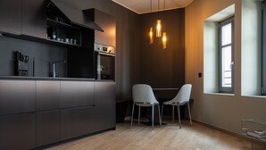 Una cucina moderna con mobili scuri, forno integrato e un'area pranzo con due sedie bianche.