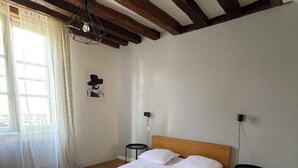 Een slaapkamer met een houten vloer, een bed met witte beddengoed, een houten hoofdbord, een hanglamp en een kleine tafel met een lamp.
