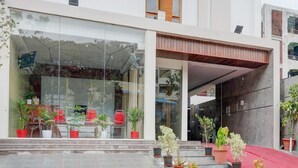 Ένα σύγχρονο κτίριο με μια γυάλινη είσοδο, φυτά σε γλάστρες και μια κόκκινη τέντα.