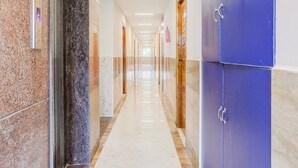 A long, well-lit hallway with marble flooring, wooden doors, and a blue cabinet. - Townhouse Sri Padmavati Ammavaari Temple (Tirupati)