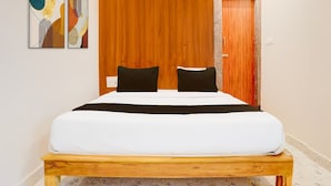 A bedroom with a bed, two black pillows, a wooden headboard, a wooden bench, and a door. - Townhouse Sri Padmavati Ammavaari Temple (Tirupati)