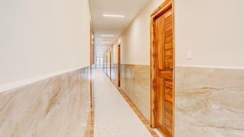 A long, narrow hallway with marble flooring, wooden doors, and recessed ceiling lighting.