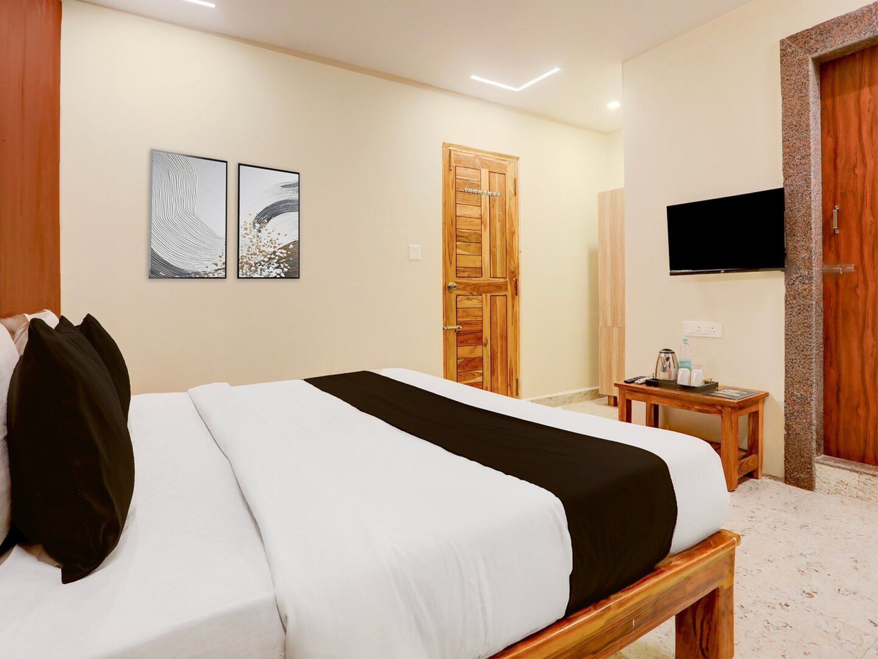 A hotel room with a bed, a wooden door, a television, and two wall-mounted artworks.