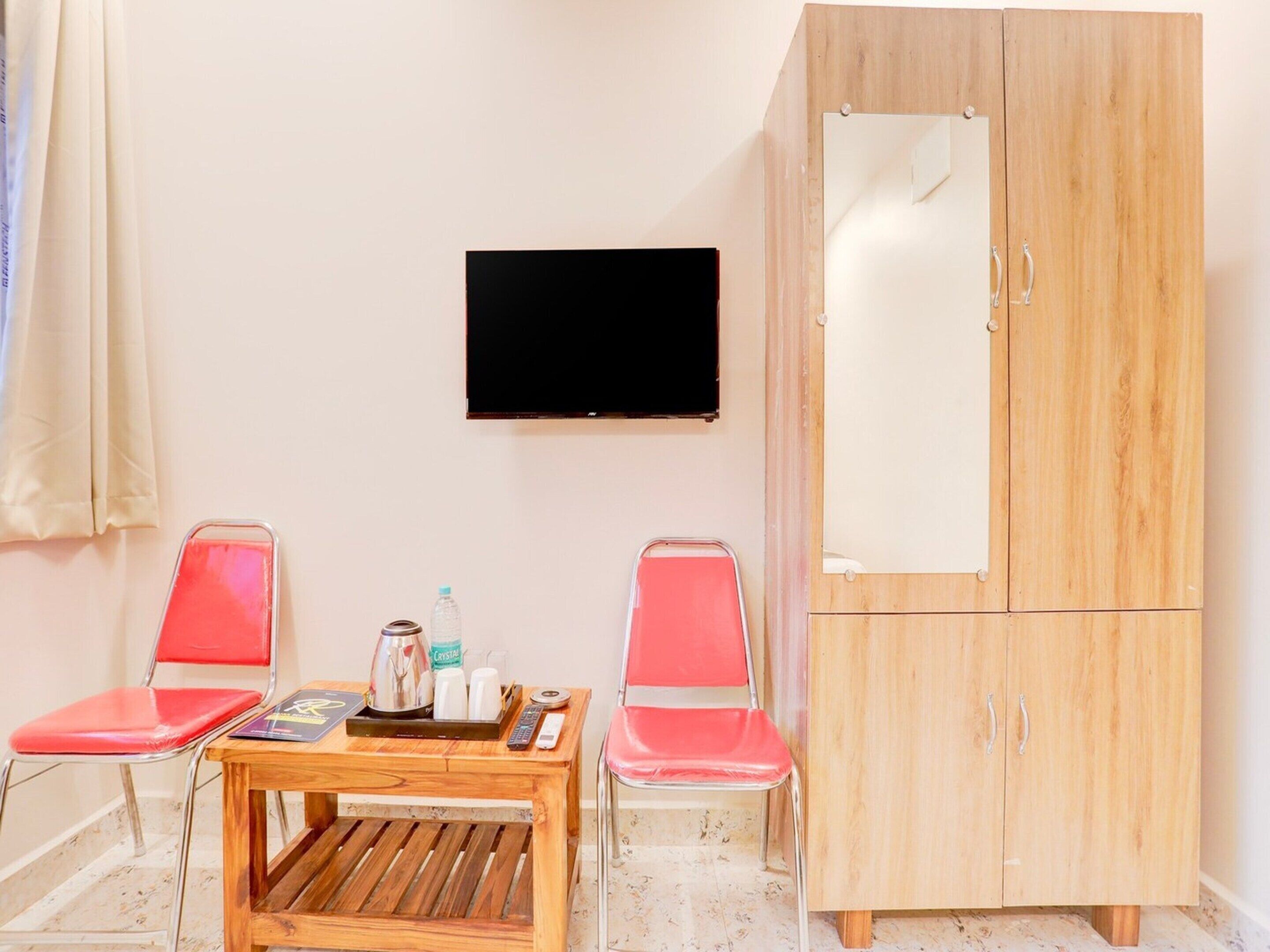 Ein Zimmer mit einem Holztisch, zwei roten Stühlen, einem an der Wand montierten Fernseher und einem Holzschrank.