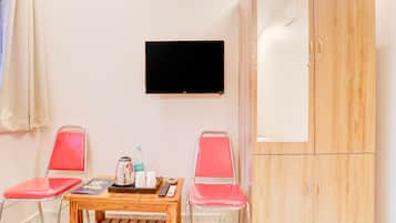 Ein Zimmer mit einem Holztisch, zwei roten Stühlen, einem an der Wand montierten Fernseher und einem Holzschrank.
