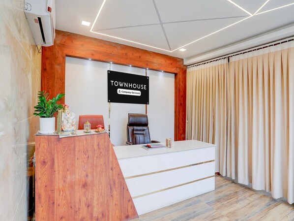 A reception desk with a sign reading 'TOWNHOUSE Company Serviced,' a potted plant, a chair, and a window with curtains.