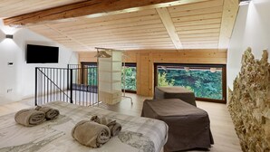 Ein modernes Schlafzimmer mit einem großen Bett, einem an der Wand montierten Fernseher und einem Balkon mit Blick auf Grünflächen.