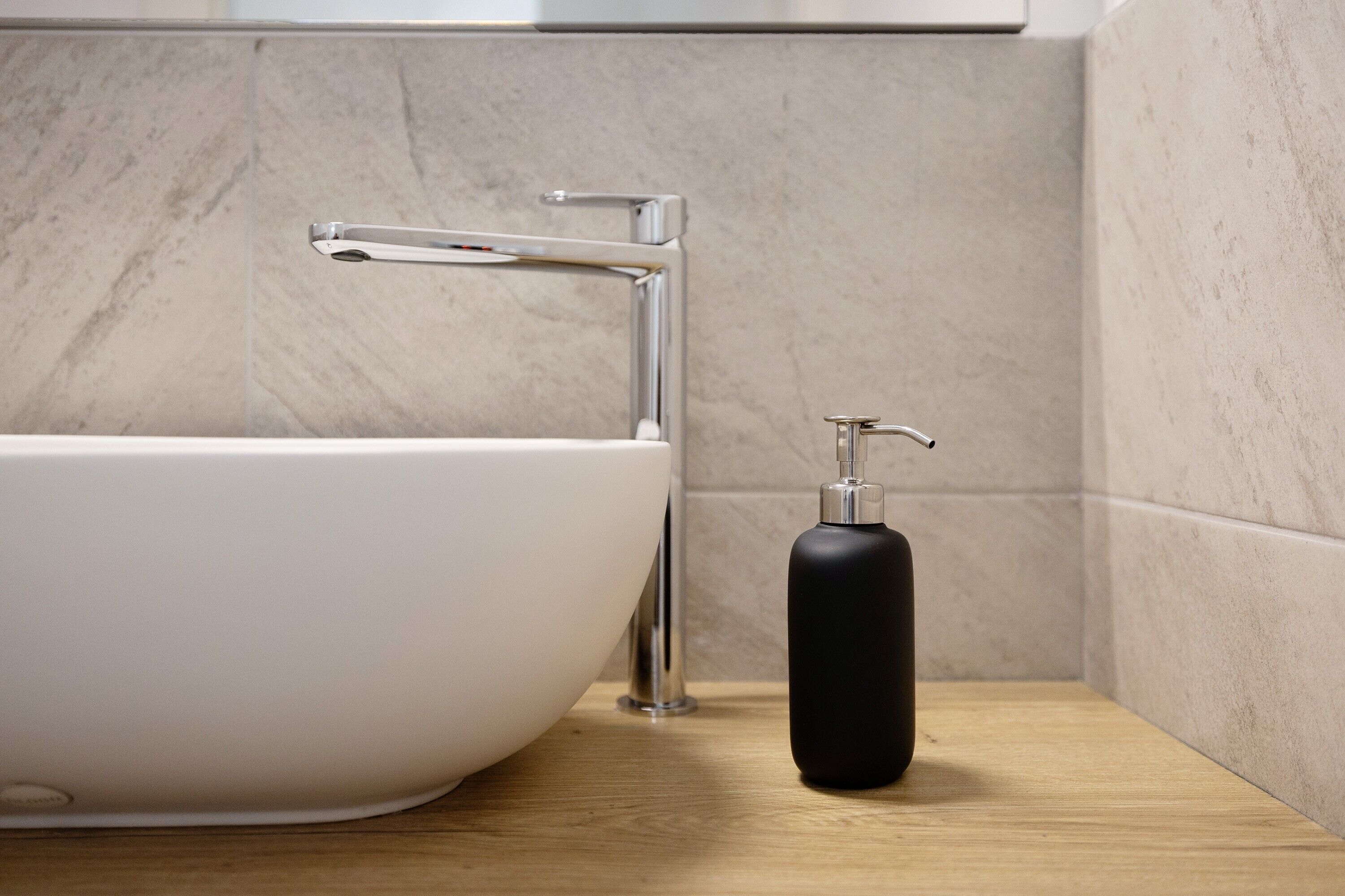 Un baño con una bañera blanca, un grifo cromado y un dispensador de jabón negro sobre una encimera de madera.