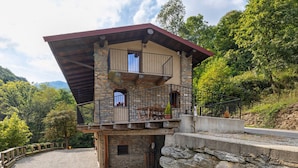 Ein Steinhaus mit Balkon, einem Schotterweg und umgebender Bepflanzung.