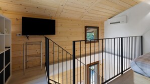 A room with a wooden ceiling, a TV mounted on the wall, a black railing, and a bed with a patterned cover. - Faunet Apartment with Mountain View, Wi-Fi and Air Conditioning (Bernezzo)