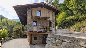 A stone building with a balcony, a gravel driveway, and surrounding greenery.