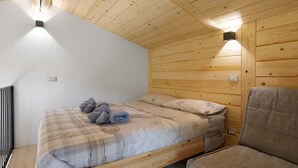 A wooden-paneled room with a bed, a chair, and a wall-mounted light fixture. - Faunet Apartment with Mountain View, Wi-Fi and Air Conditioning (Bernezzo)